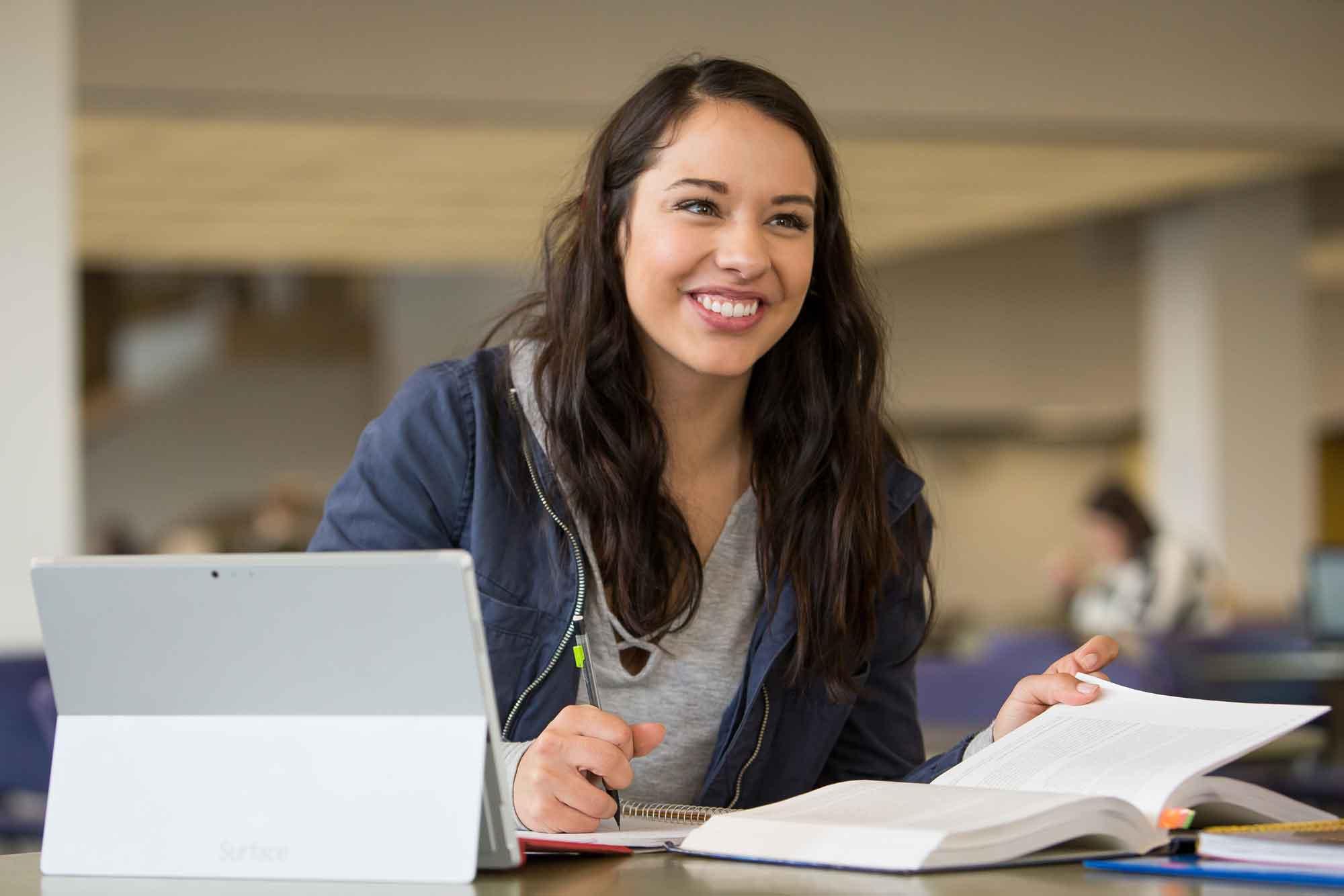 转移 student sitting at work desk on UNC campus with a book an ipad.